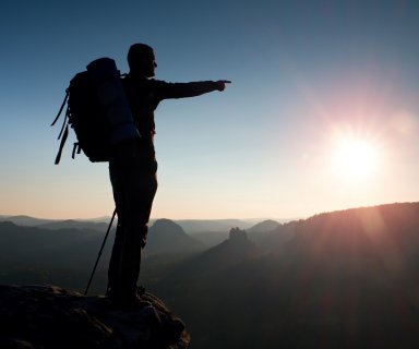 Sharp silhouette of a tall man on the top of the mountain with sun in the frame. Tourist guide in mountains